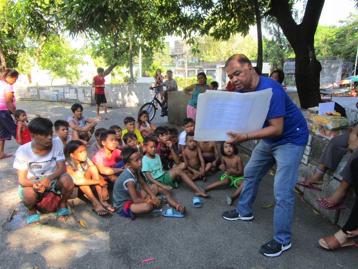フィリピンの路上で紙芝居をする人とそれを見る子どもたち