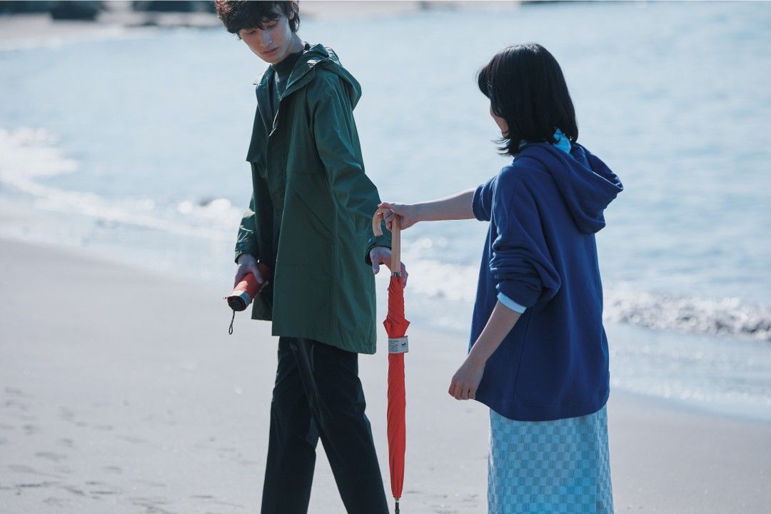 傘を持って海辺を歩く男女