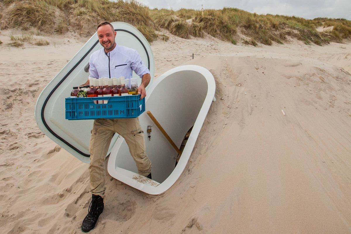 砂浜に埋められた「Groundfridge(グランドフリッジ)」から、飲料をカゴに入れて出てくる男性