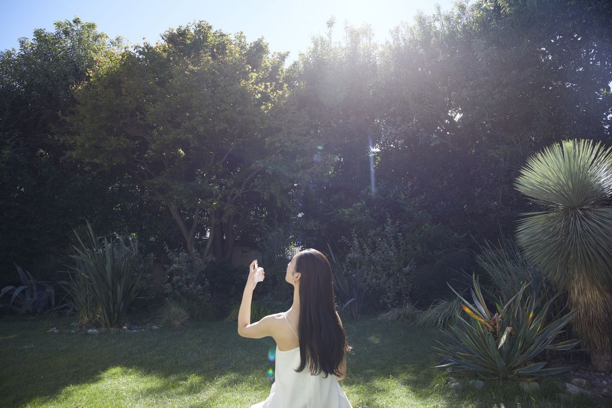 木漏れ日の中でスキンケアアイテムを使う女性