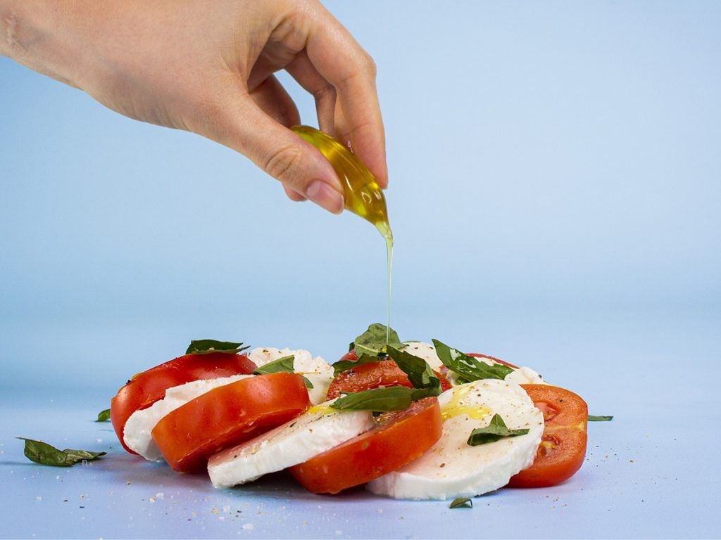 ノットプラに入ったオリーブオイルをカプレーゼに垂らす様子