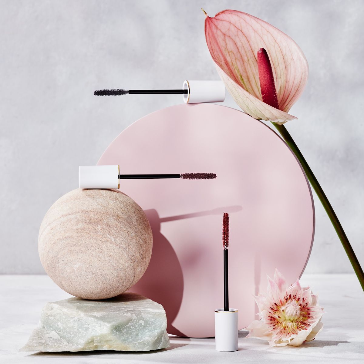 「トーン ロング ラッシュ マスカラ」、花、石を並べた写真